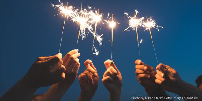 Six hands holding sparklers against the sky