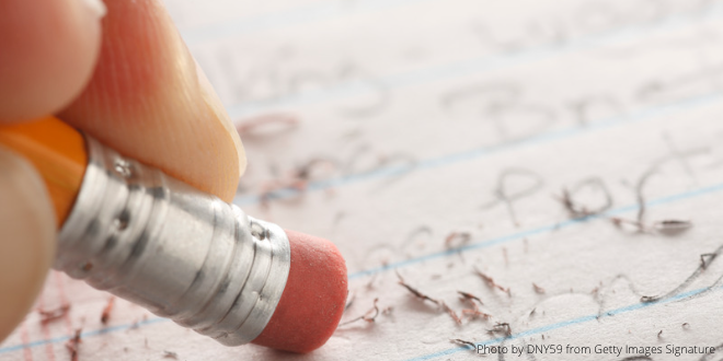 A close-up of the tip of a pencil with an eraser on it, erasing hand-written notes