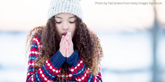 A young lady wearing a thick jumper and a woollen hat, rubbing her hands to keep warm