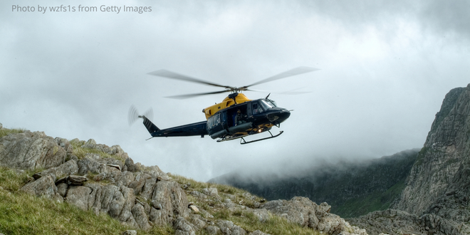 A mountain rescue helicopter flying over the hills