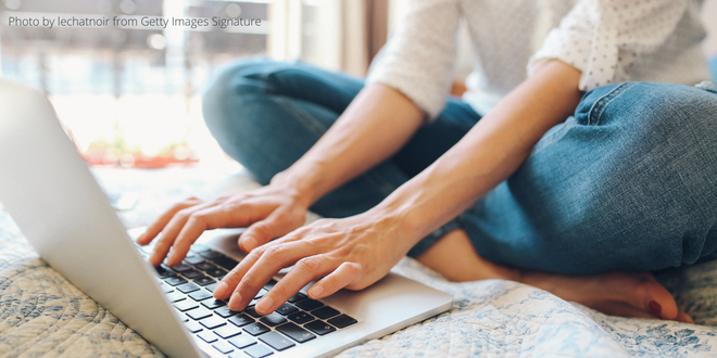 A young woman sitting cross-legged in front of her laptop and writing on her keyboard