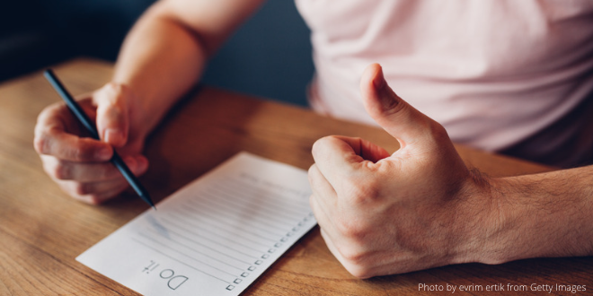 A close-up of a man sitting at his desk with a note pad in front of him