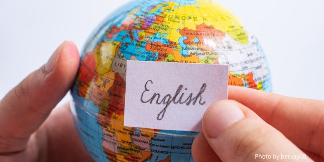 A hand holding a globe and another hand holding a piece of paper in front of it with the word "English" on it.