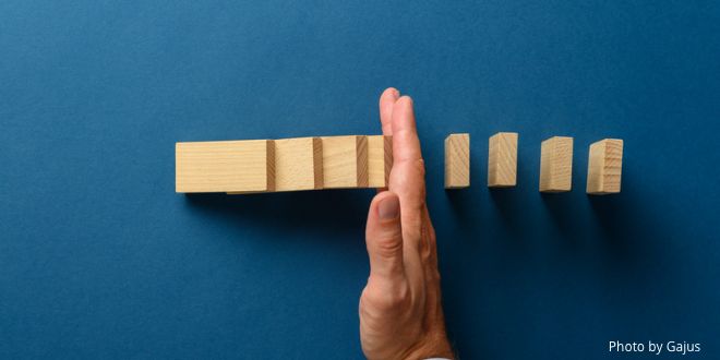 Small wooden bricks on a blue background and a hand stopping them all falling onto one another (a domino effect)