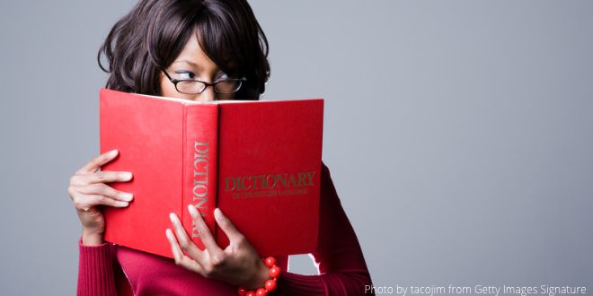 A young woman holding a red English dictionary in front of her face, but looking to the side