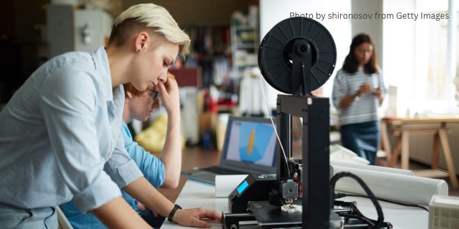 A young woman working on a piece of equipment with two other people in the background