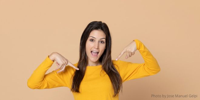 A young lady wearing a yellow jumper pointing to herself