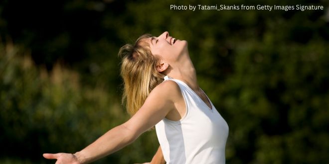 A young woman looking into the sky with her arms stretched out behind her back