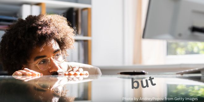 An African American man peeping over his desk looking at the word "but"