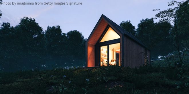 A tiny house surrounded by trees with its lights on