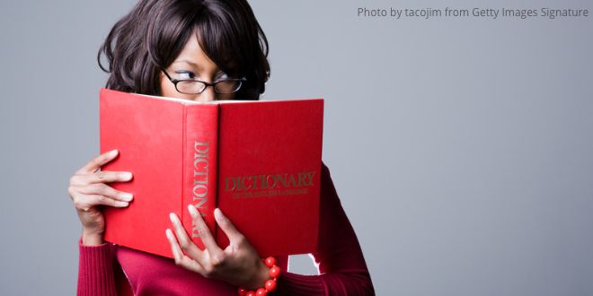 A young woman holding a red dictionary, with her eyes peeping over it