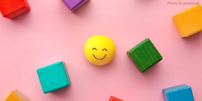 A yellow smiley ball and lots of different coloured wooden cubes on a pink background