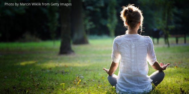 A young woman sitting on the grass with her back to us, meditating