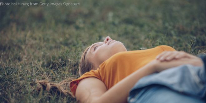 A young woman wearing an orange T-shirt, lying in the grass