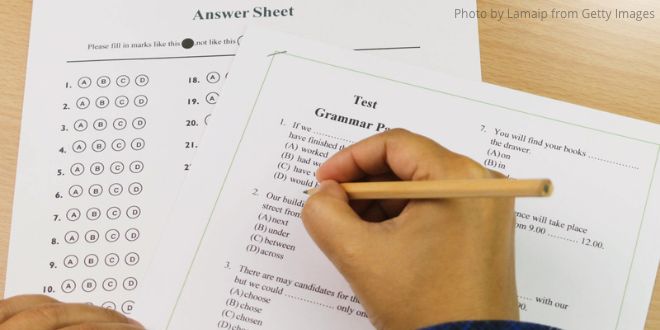 A hand filling in an English grammar test with an answer sheet on the table