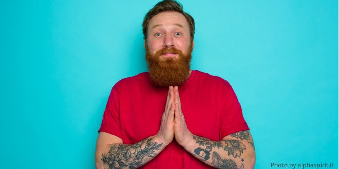 A man in a red T-shirt with his hands in front of him as in prayer