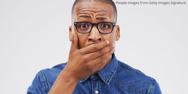 A young man with his hand over his mouth, looking shocked