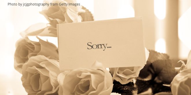 A bunch of white roses on table with a little note carrying the words "Sorry"