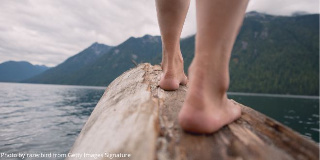 A close-up of the feet and lower legs of someone ready to jump from a rock into a lake or river