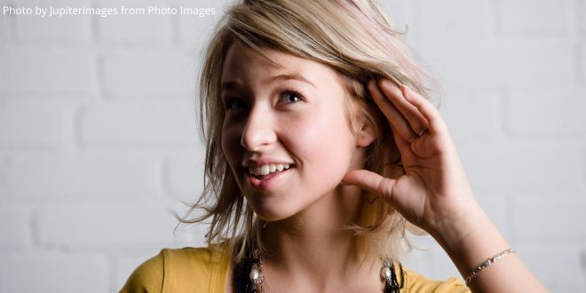 A close-up of a young lady with her left hand behind er left ear as if listening closely to someone or something