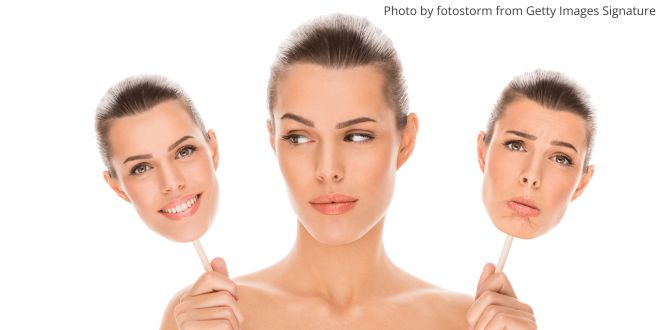 A woman holding two masks, one with a happy face and one with a sad one