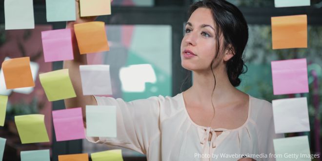 A woman writing on Post-it notes fixed onto a glass wall