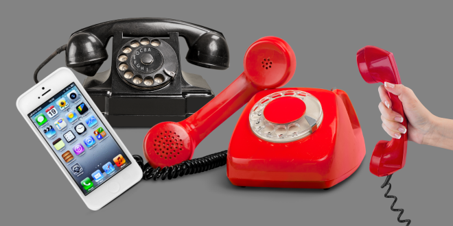 An old black and an old red telephone, a mobile phone and a hand holding a red receiver