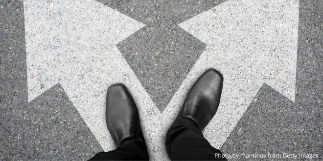 A pair of black shoes standing on two arrows—one pointing towards the left and the other pointing towards the right