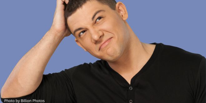 A man wearing a black t-shirt, scratching his head as if thinking