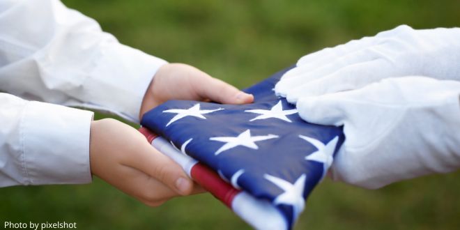 Two pairs of hands holding an American folded flag