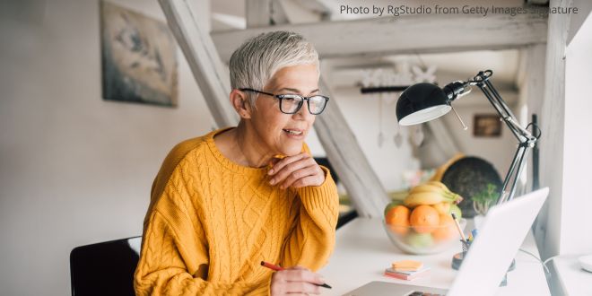 A grey-haired woman sitting at her desk working