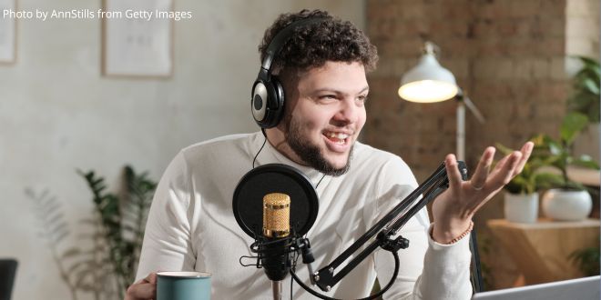 A young man with headphones sitting in front of a microphone and recording his voice