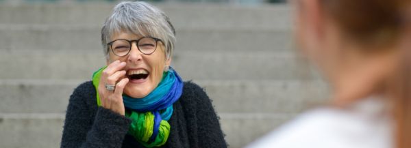 Christine Burgmer sitting on steps in the Media Park, and laughing with a client.