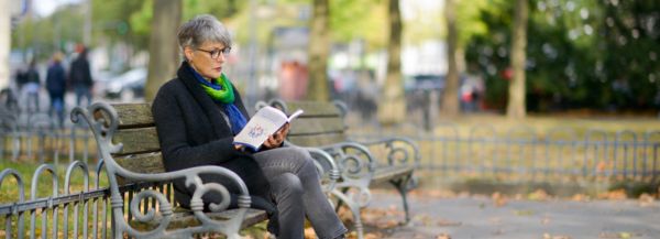 Christine Burgmer sitting on a park bench, reading an English book and waiting for a client.