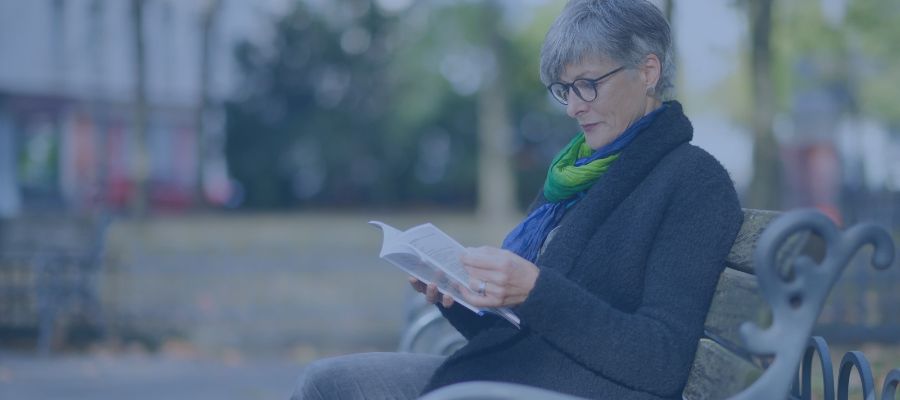 Aussprache Christine Burgmer sitzt auf einer Parkbank in Köln und liest.